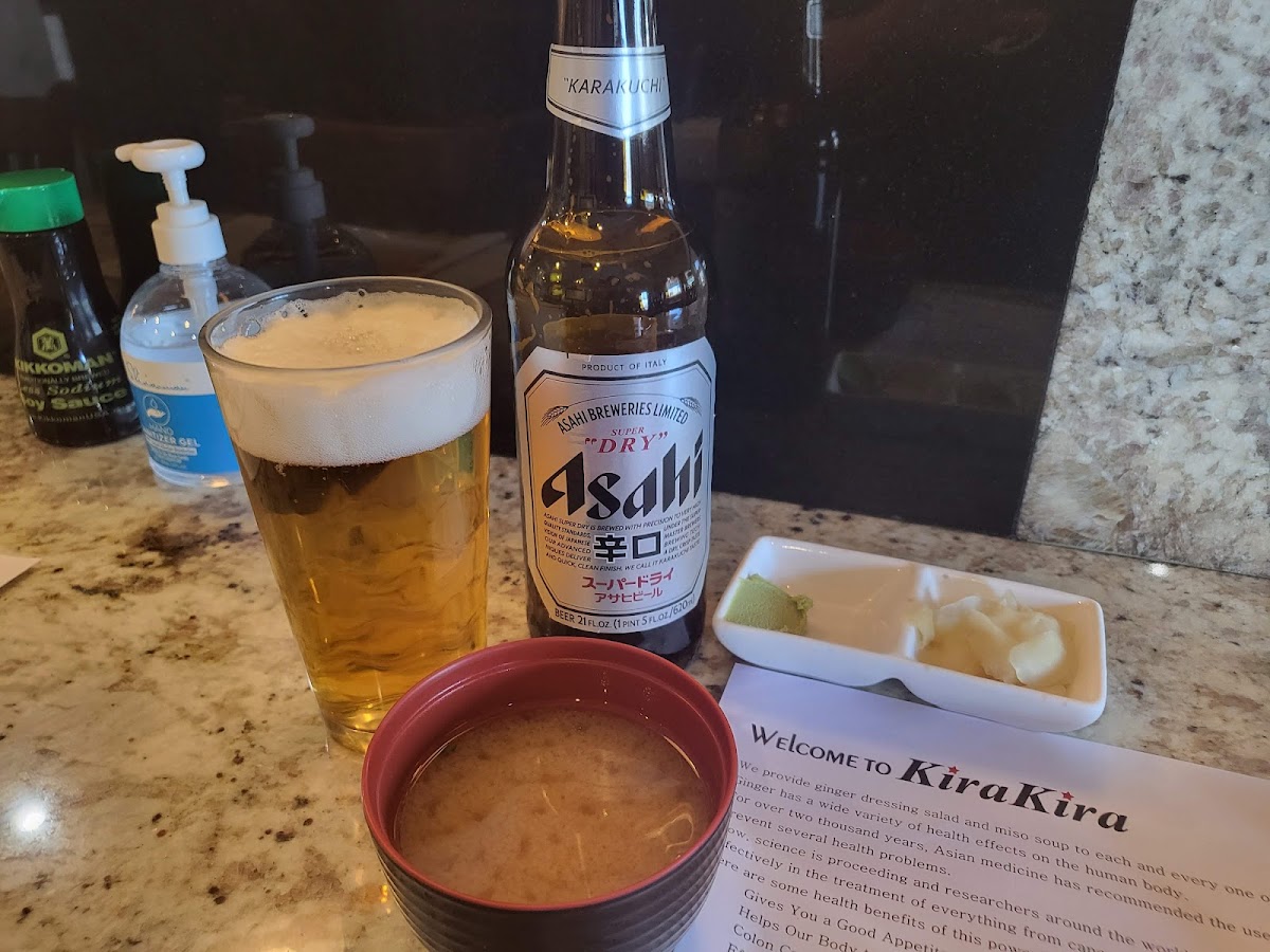 A poured Asahi beside a bottle of Asahi Super Dry, a bowl of miso soup and the restaurant's welcome card on the counter