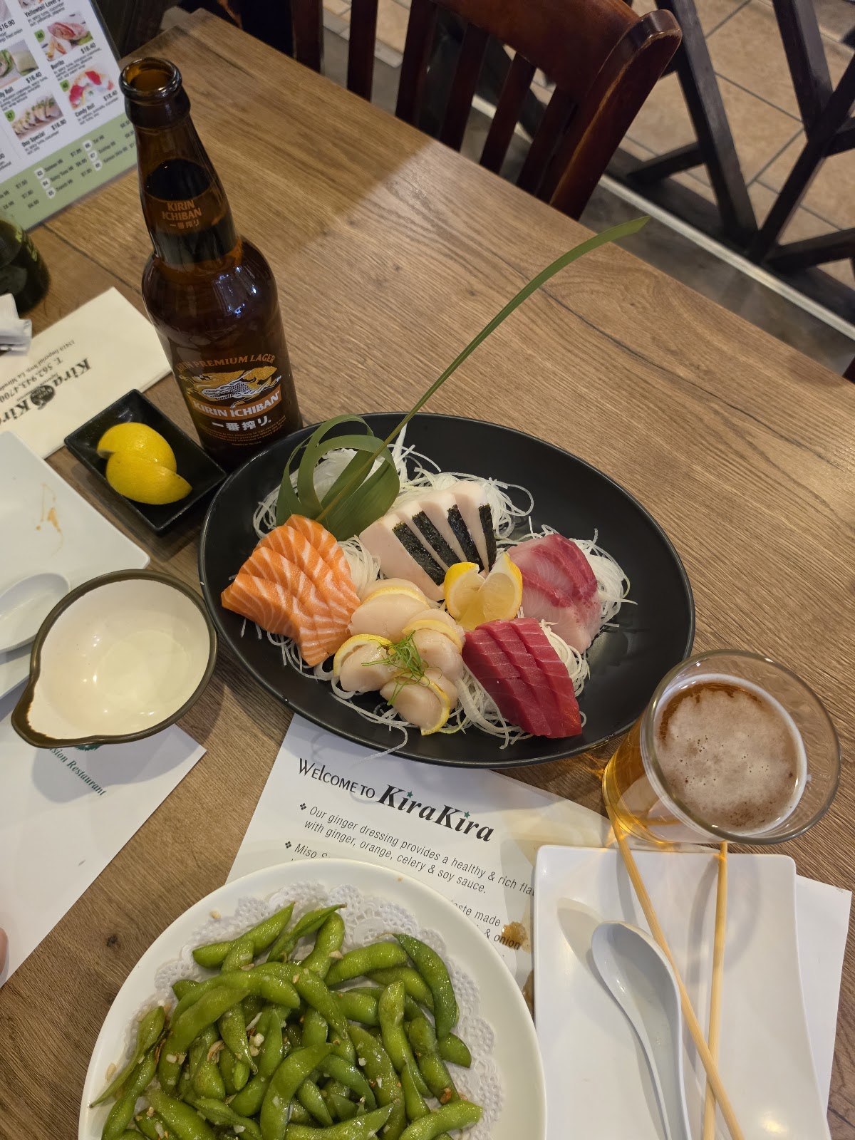 A sashimi plate with a bottle of Kirin Ichiban and a dish of edamame on the table