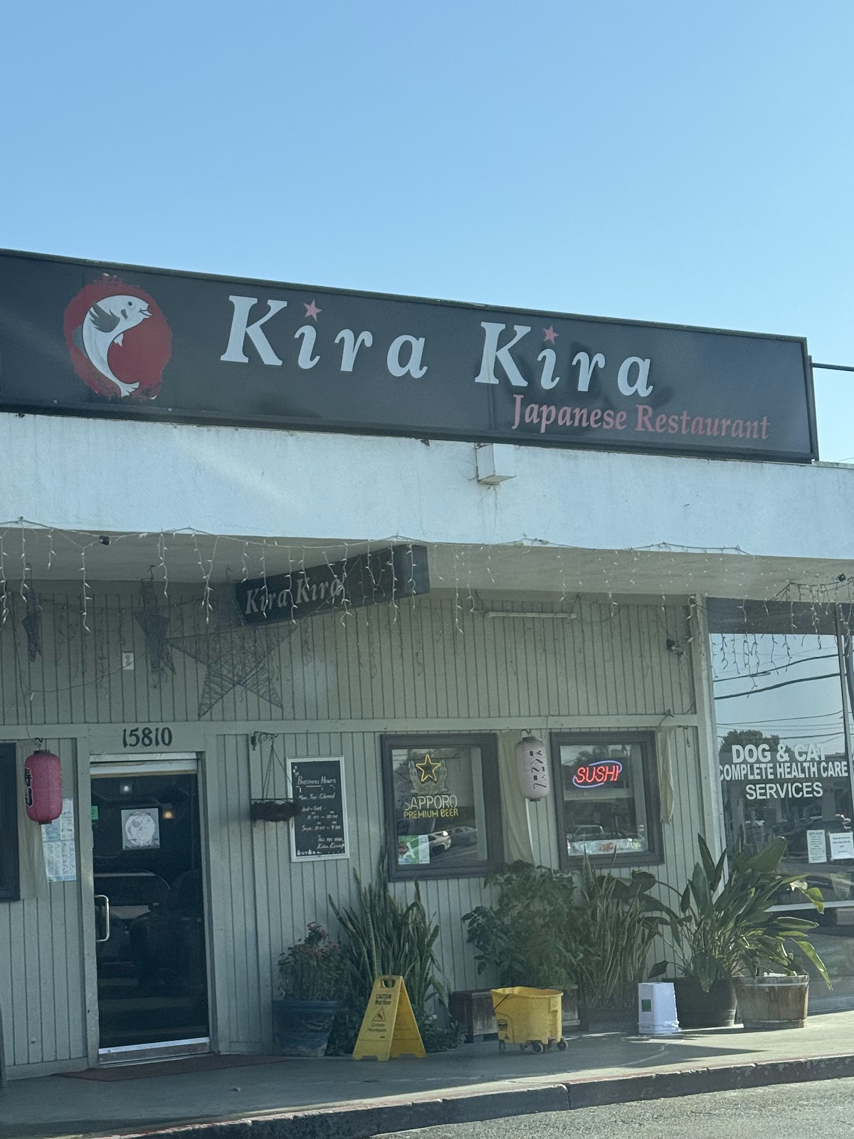 Kira Kira's storefront in daylight, with the painted sign, hanging lantern and hours posted on the door